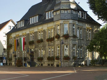 Rathaus_01©Tourist-Information Lage.jpg Historisches Rathaus mit markanter Architektur und Blumenschmuck, umgeben von Kopfsteinpflaster.