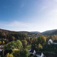 Herbstliche Landschaft mit am Waldrand; Blick über Wohnsiedlung mit Bäumen unter strahlend blauem Himmel.