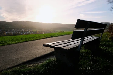 Aussichtspunkt Eine Holzbank steht am Wegesrand mit Blick über ein Dorf, beleuchtet von der Abendsonne.