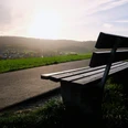Aussichtspunkt Eine Holzbank steht am Wegesrand mit Blick über ein Dorf, beleuchtet von der Abendsonne.