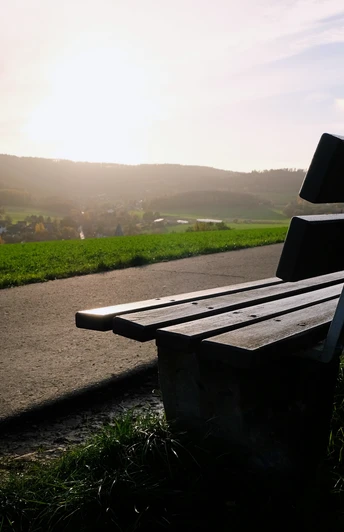 Aussichtspunkt Eine Holzbank steht am Wegesrand mit Blick über ein Dorf, beleuchtet von der Abendsonne.