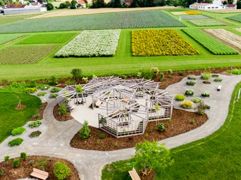 Ein Holzpavillon steht inmitten sorgfältig angelegter Beete auf einem weitläufigen Kräuterfeld.