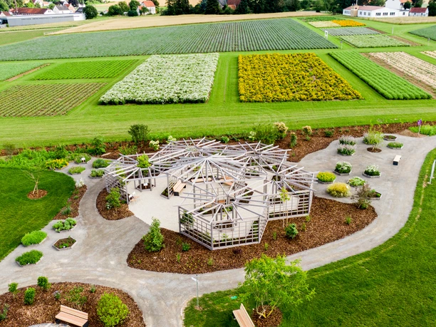 2021-07-15-taoasis-0931©TAOASIS.jpg Ein Holzpavillon steht inmitten sorgfältig angelegter Beete auf einem weitläufigen Kräuterfeld.