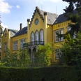 Ein gelbes Herrenhaus mit stilvollen Giebeln, grüner Fassade und reich bewachsenen Gartenanlagen.