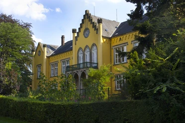 Schloss_Iggenhausen_von_vorne_01©Tourist-Information Lage.jpg Ein gelbes Herrenhaus mit stilvollen Giebeln, grüner Fassade und reich bewachsenen Gartenanlagen.
