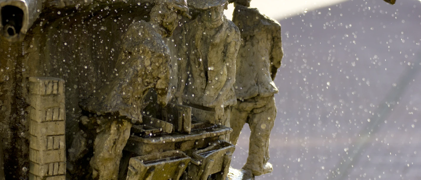 Marktplatz_Brunnen_Detail_01©Tourist-Information Lage.jpg Wasser spritzt aus einem kunstvoll gestalteten Brunnen mit detailreichen Figuren in enger Interaktion.