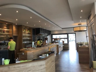 Modernes Café mit Holztresen, großen Fenstern und zwei Beschäftigten in grünen Hemden.