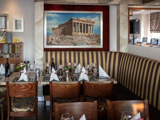 Innenansicht eines Restaurants mit gedecktem Tisch, darüber ein Wandbild der Akropolis.