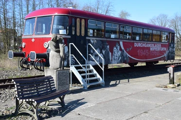 historischer Schienenbus Ein roter, historischer Zug steht auf einem Gleis. Neben dem Zug befindet sich eine steinerne Skulptur einer Frau.