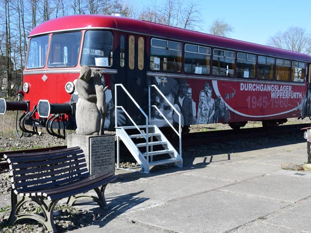 historischer Schienenbus Ein roter, historischer Zug steht auf einem Gleis. Neben dem Zug befindet sich eine steinerne Skulptur einer Frau.
