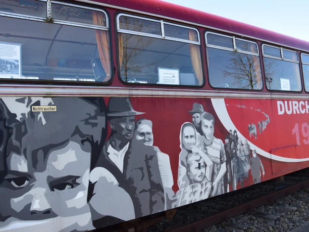historischer Schienenbus Historischer Zugwaggon mit beeindruckender Wandmalerei, die Menschen in historischen Szenen darstellt.