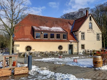 Historische Obere Mühle mit roten Dachziegeln, Terrasse, schneebedecktem Boden und winterlicher Kulisse.