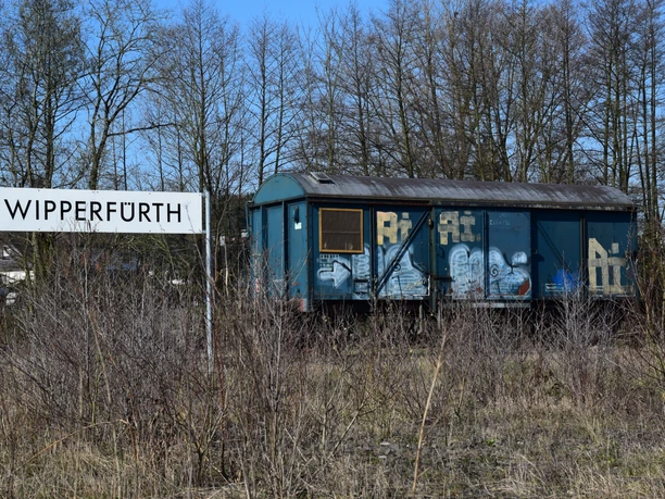 Ein verlassener blau-grauer Güterwaggon steht vor kahlen Bäumen in Wipperfürth.