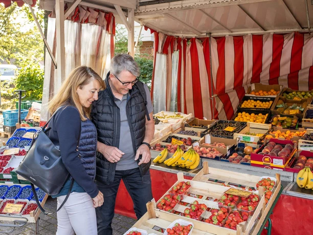 wochenmarkt-bad-zwischenahn.jpg Ein Mann und eine Frau sehen sich lächelnd die frischen Obststände auf einem Wochenmarkt an.