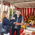 wochenmarkt-bad-zwischenahn-obst.jpg Ein Wochenmarktstand mit frischem Obst: Verkäufer reicht einer Kundin lächelnd Erdbeeren.