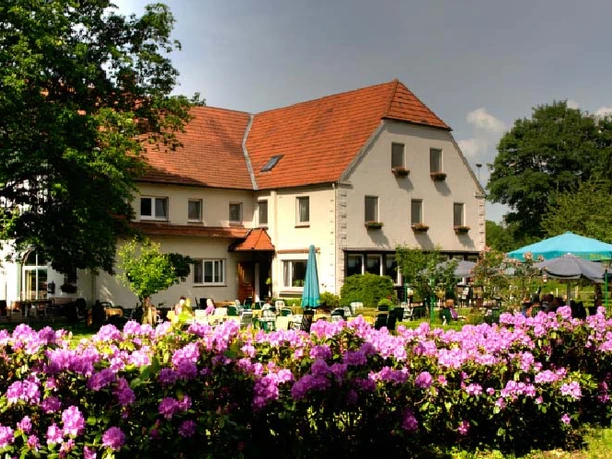 Ein großes Haus mit rotem Satteldach, umgeben von blühenden Rhododendren unter freiem Himmel.