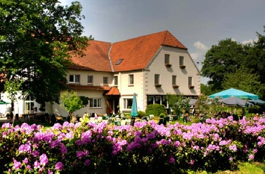 Landhaus Röscher Ein großes Haus mit rotem Satteldach, umgeben von blühenden Rhododendren unter freiem Himmel.