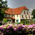 Landhaus Röscher Ein großes Haus mit rotem Satteldach, umgeben von blühenden Rhododendren unter freiem Himmel.