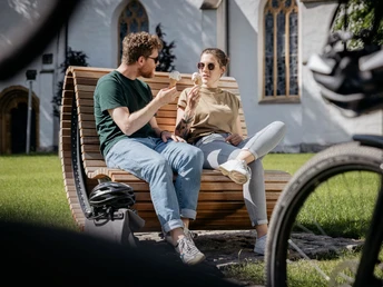 Ein Paar sitzt auf einer Holzbank im Park und genießt Eis, mit Fahrrädern im Vordergrund.