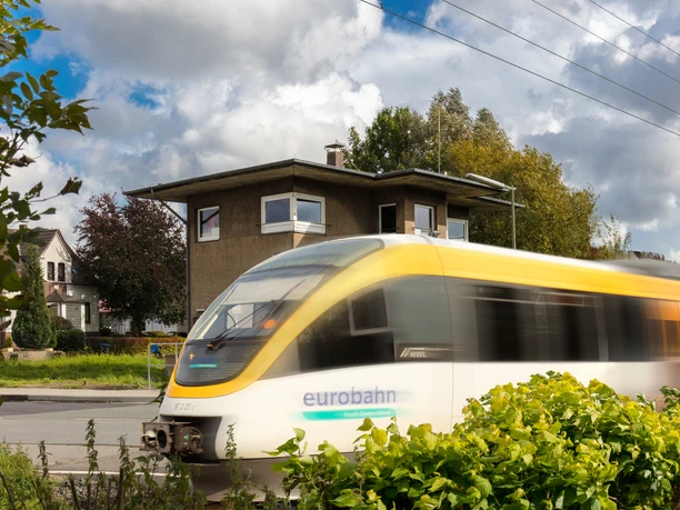 Ein vorbeifahrender Eurobahn-Zug passiert ein Wohngebiet mit modernen Häusern und grüner Vegetation.