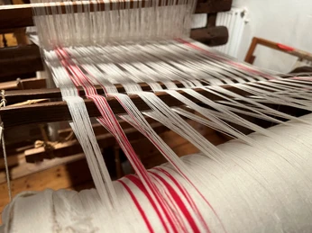 Webstuhl Historischer Webstuhl zeigt komplexe, kontrastreiche Verknüpfung von weißen und roten Fäden.