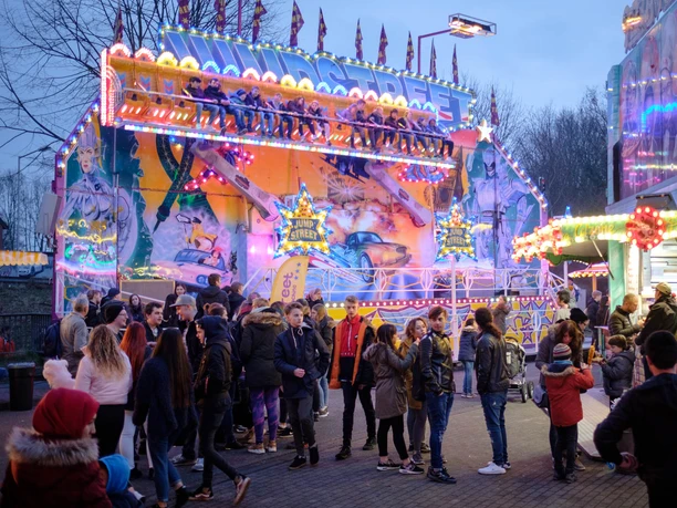 Vlothoer Brückenmarkt Jumpstreet Menschenmenge vor einer leuchtenden, bunten Kirmesattraktion in der Dämmerung mit Jugendlicher.