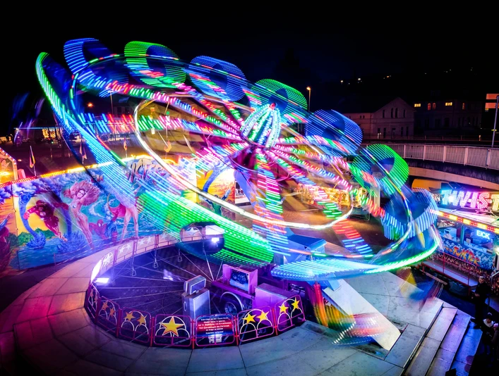 Brückenmarkt Vlotho Leuchtendes Karussell vor nächtlicher Kulisse, umgeben von bunten Ständen und Lichtern.