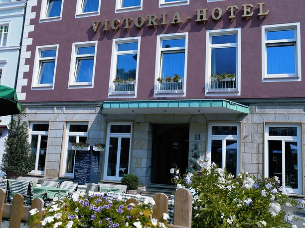 Fassade des Victoria Hotels mit blühenden Blumen im Vordergrund und klassischer Architektur.