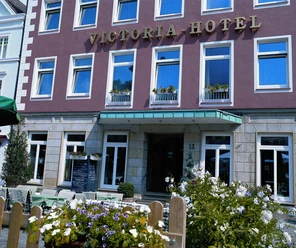 Aussenansicht.jpg Fassade des Victoria Hotels mit blühenden Blumen im Vordergrund und klassischer Architektur.