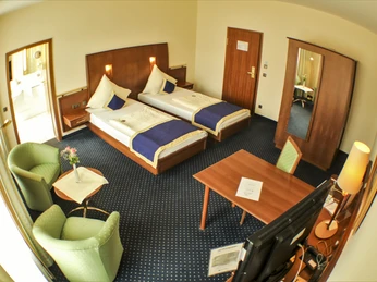 Zwei Einzelbetten in einem geräumigen Hotelzimmer mit Holzmöbeln, zwei Sesseln und Schreibtisch.