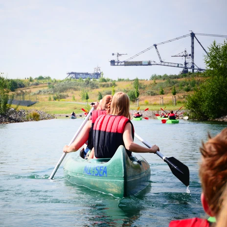 Kajakarze z kamizelkami ratunkowymi wiosłujący po jeziorze Markkleeberg, w tle zabytek przemysłowy Bergbau-Technik-Park, wypoczynek, sporty wodne, kajakarstwo, aktywny