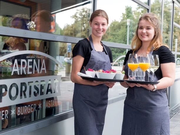 Arena Sportsbar - Gastronomie in Leipzig Zwei junge Servicekräfte mit Tablett stehen vor der Sportsbar der Arena Leipzig in der Veranstaltungen im Sport bei einem Getränk in gemeinsamer Gruppe erlebt werden können, Freizeit, Gastronomie