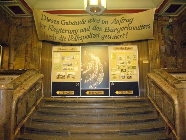 Treppenaufgang im Museum in der Runden Ecke - Friedliche Revolution in Leipzig Blick vom unteren Ende des Treppenaufgangs auf mehrere Banner und Poster, die auf das Museum in der Runden Ecke hindeuten, Friedliche Revolution, Geschichte, Freizeit, Sehenswürdigkeiten
