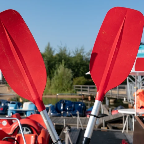 Dwa czerwone wiosła przecinające się, w tle rowery wodne na wypożyczalni, leipziger neuseenland, aktywne, sporty wodne