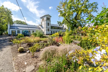 Leipzig Botanical Garden - Leisure facility in Leipzig View of the plant world of the botanical garden, with green beds in the foreground and one of the buildings in the background; summer, blue sky, flowers