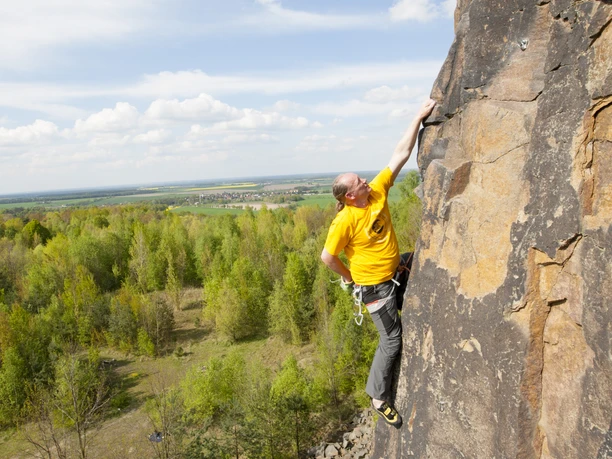 Klettern in den Steinbrüchen - Aktiv in der Leipzig Region Ein Mann klettert einen Steinbruch hinauf, im Hintergrund Natur und eine Ortschaft, Aktiv, Klettern, Natur