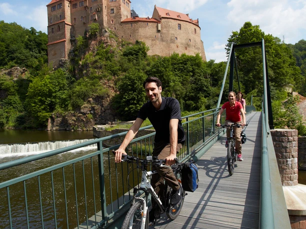 Dva cyklisté jedou přes most přes Zschopau, v pozadí hrad Kriebstein, cyklostezky