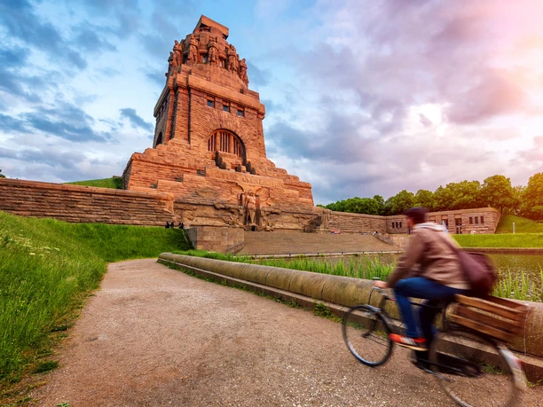 View of the Völkerschlachtdenkmal Leipzig, illuminated by the warm sun, while a cyclist cycles past the Lake of Tears, a real sight and a special piece of architecture in Leipzig, Excursion, Sights, Culture