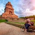 Völkerschlachtdenkmal - Sehenswürdigkeiten in Leipzig Blick auf das von der warmen Sonne angestrahlte Völkerschlachtdenkmal Leipzig, während ein Fahrradfahrer am See der Tränen vorbeiradelt, eine wahre Sehenswürdigkeit und ein besonderes Stück der Architektur in Leipzig, Ausflug, Sehenswürdigkeiten, Kultur
