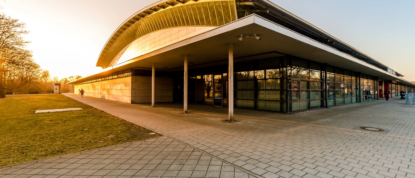 Wejście do QUARTERBACK Immobilien ARENA Leipzig w wieczornym słońcu, które jest wykorzystywane jako obiekt sportowy, ale także jako scena i miejsce wydarzeń, takich jak koncerty.