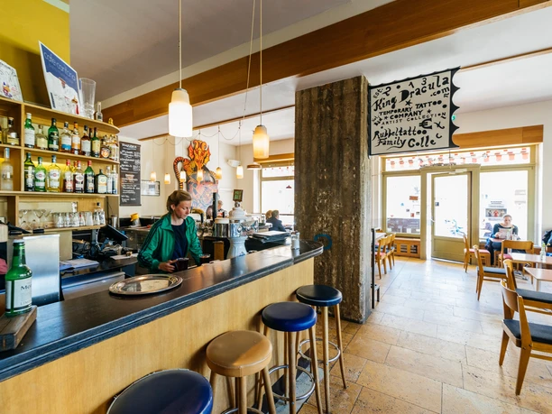 Jadalnia Café Cantona z długim barem i stołkami barowymi oraz dużym oknem frontowym z widokiem na Windmühlenstraße.