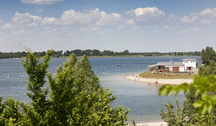 Pomiędzy zielonymi drzewami widać jezioro Schladitz i brzeg plaży