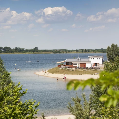 Pomiędzy zielonymi drzewami widać jezioro Schladitz i brzeg plaży