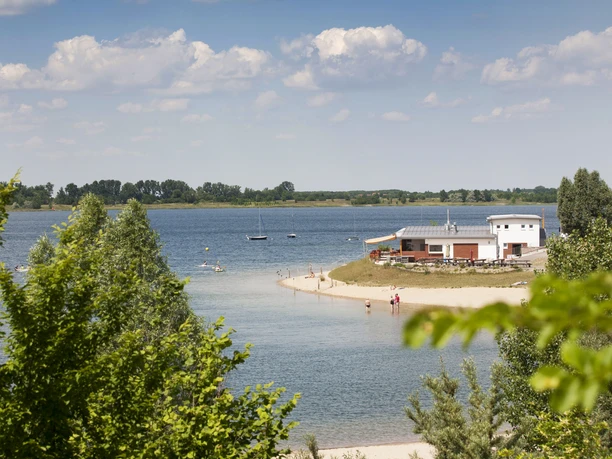 Entre les arbres verts, on a une vue sur le lac Schladitzer et la plage.