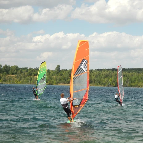 Trois véliplanchistes se tiennent debout sur leurs planches dans la houle du lac de Schladitz