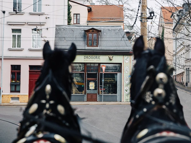 Drogerie - Gastronomie v Lipsku Pohled na vnější fasádu restaurace Drogerie v Lipsku s tažnými koňmi a tramvají v popředí