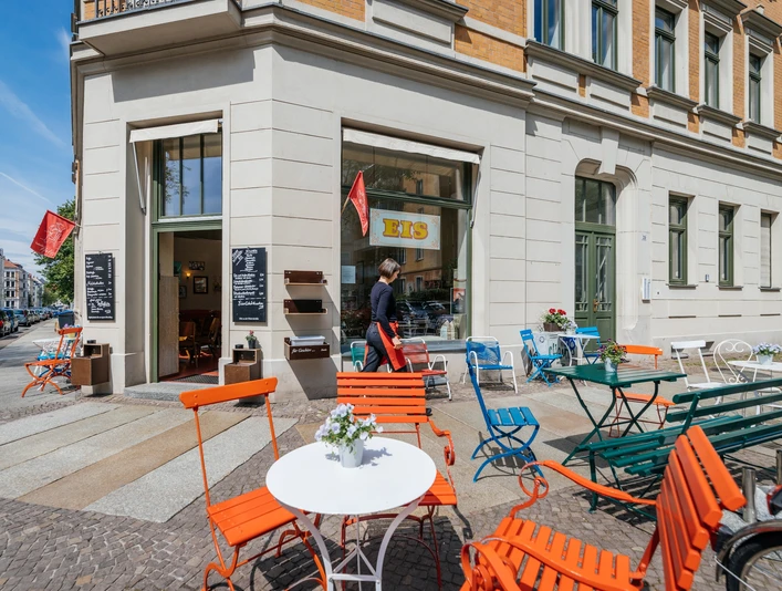 Eisdiele Pfeifer - Eisdielen in Leipzig Blick auf den Freisitz der Eisdiele Pfeifer mit verschiedenen Gartenmöbeln und Fassade im Gründerzeitstil, freize