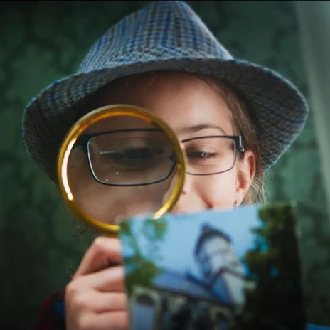 Ein Kind mit Detektivhut untersucht mit der Lupe ein Foto im Escape Room.