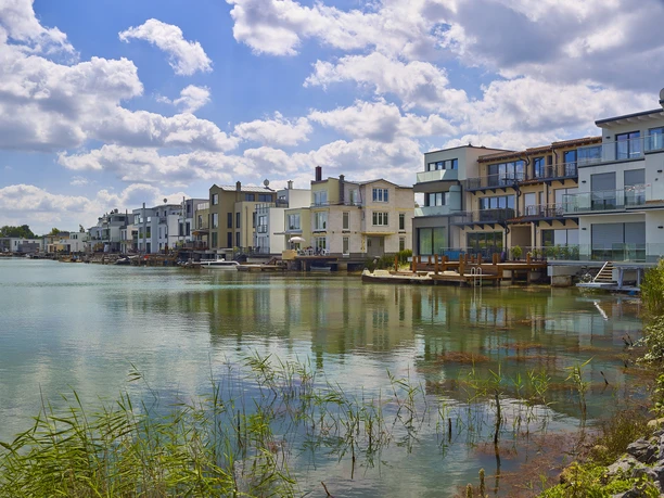 Des habitations modernes avec de grandes fenêtres et des balcons se reflètent dans les eaux calmes de la lagune de Kahnsdorf.