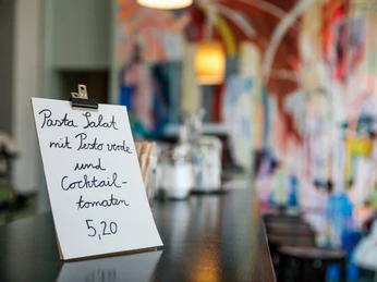 INO Café - Cafés in Leipzig Detailaufnahme eines sich auf der Theke befindlichen Schildes; verschwommen im Hintergrund ist bunte Wandbemalung zu erkennen, gastronomie, cafe, restaurant